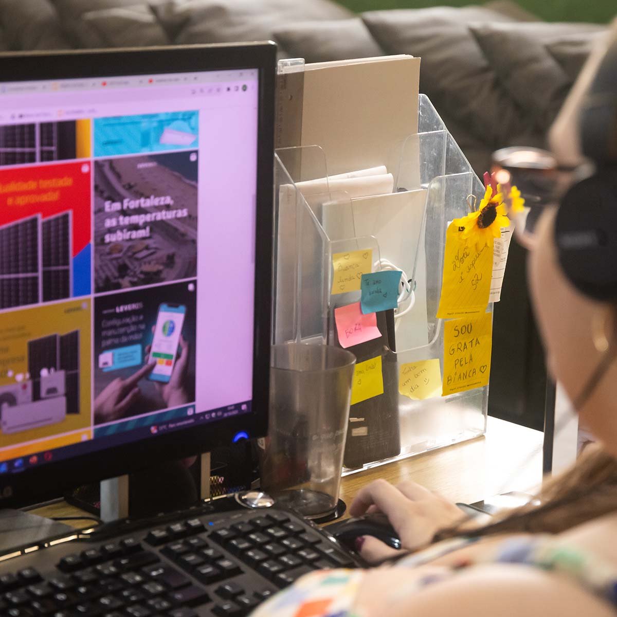 Integrante da equipe do Grupo Dls/ revisando peças de campanha na tela do computador, com recados em post-it ao lado do monitor