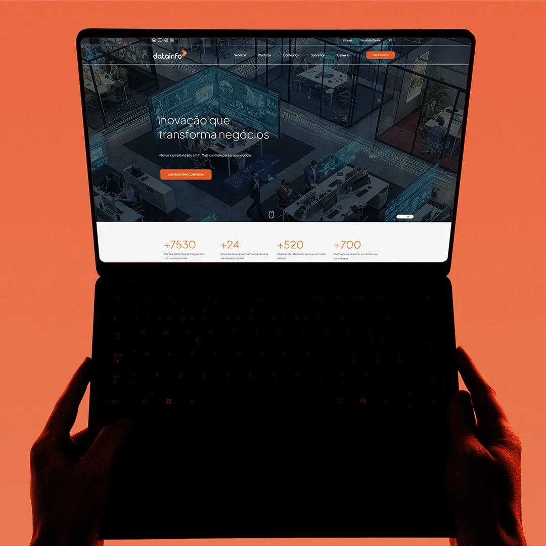 Notebook inclinado sobre uma base clara, com a home da Datainfo aberta na chamada “Inovação que transforma negócios” e a faixa de números do site logo abaixo.