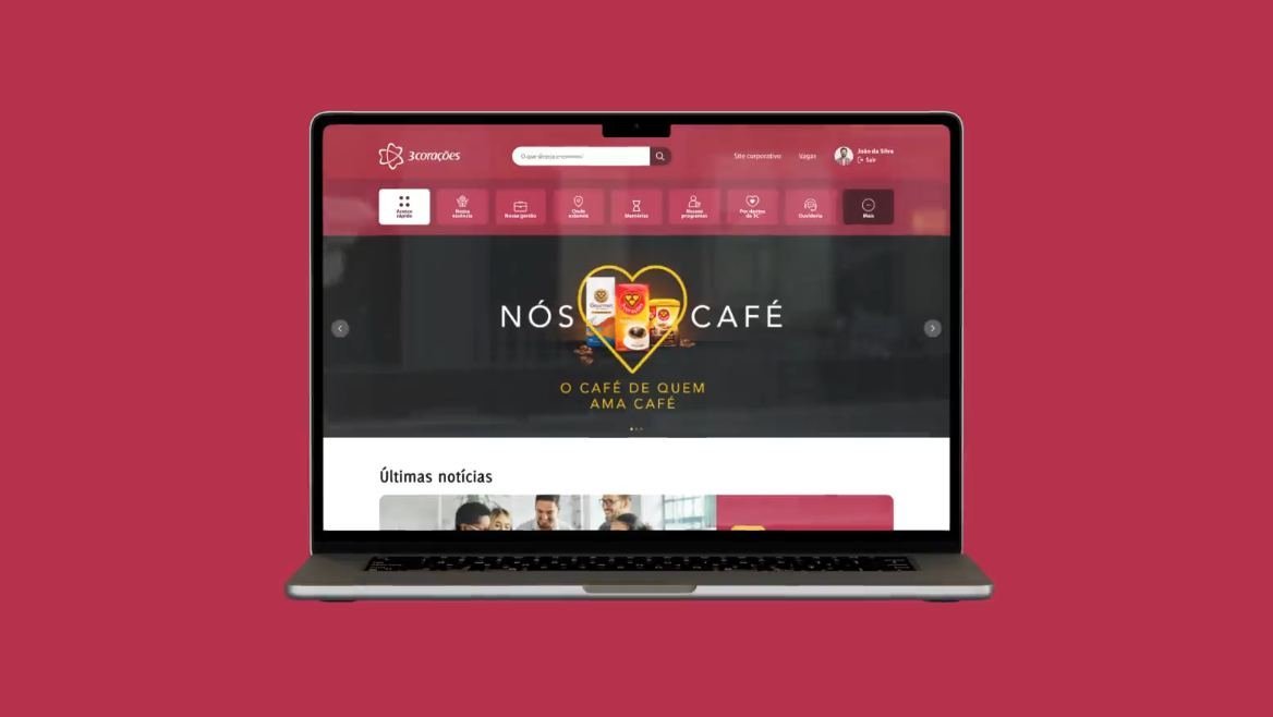 Notebook sobre fundo vermelho mostrando a home da intranet, com o menu de acesso rápido e o banner “Nós amamos café”