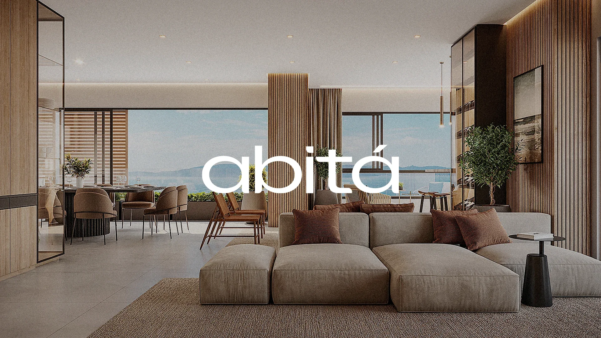 Render de uma sala de estar com sofá modular, mesa de jantar e vista para o mar, com a assinatura abitá em branco sobre a imagem.