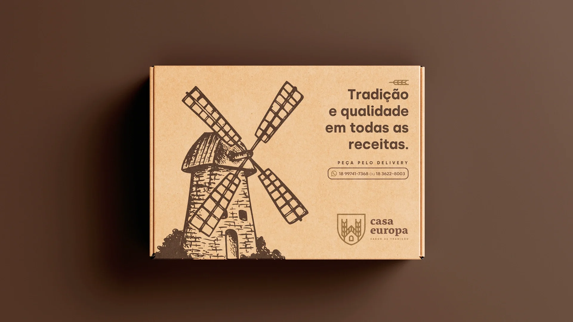 Caixa de delivery em papelão kraft com o moinho impresso em marrom, a frase “Tradição e qualidade em todas as receitas”, os telefones do delivery e a assinatura Casa Europa.