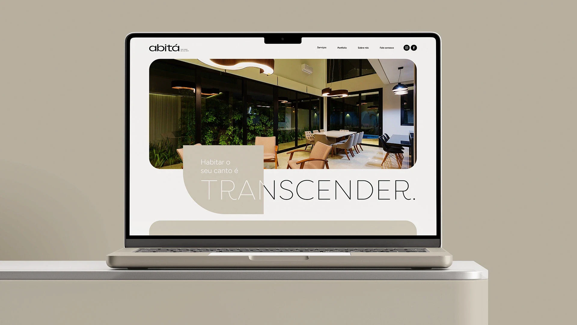 O site da Abitá num notebook: a foto de um interior com jardim vertical e pé-direito alto, e a chamada “Habitar o seu canto é transcender.”.