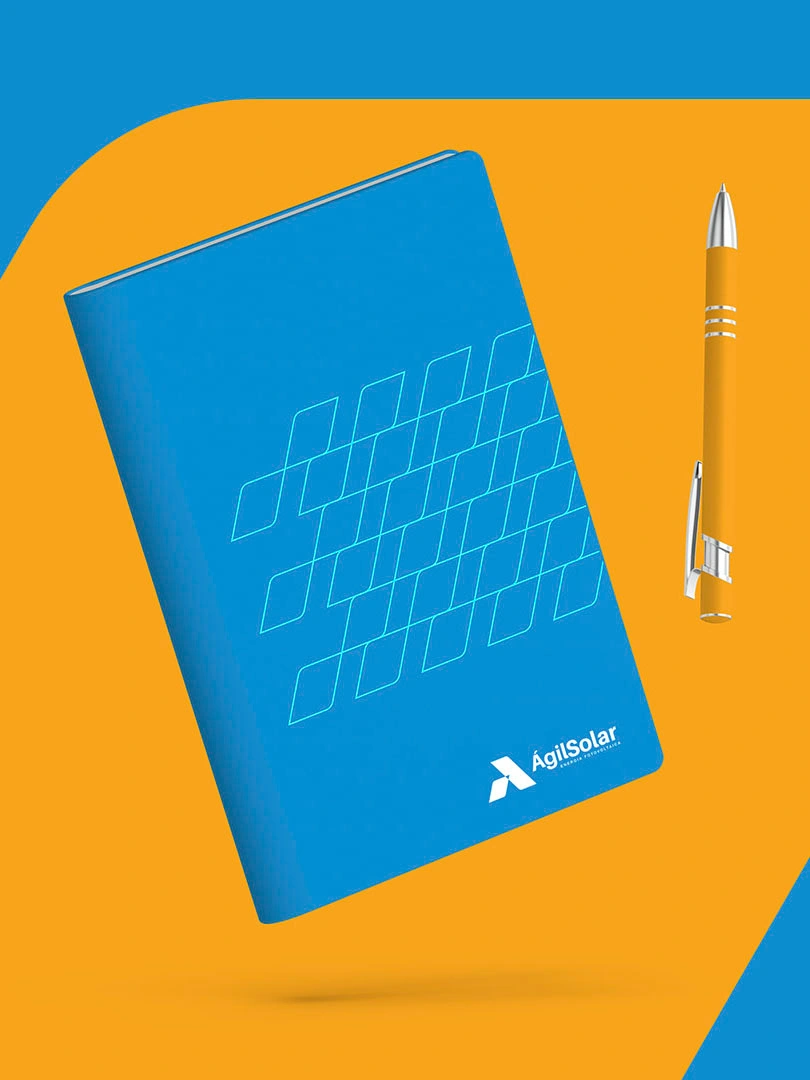 Caderno azul com a malha de placas em linha e a assinatura da Ágil Solar, ao lado de uma caneta laranja, sobre fundo laranja e azul.