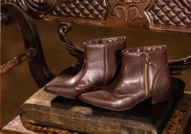 Par de botas marrons de cano curto sobre um banco antigo de madeira entalhada.