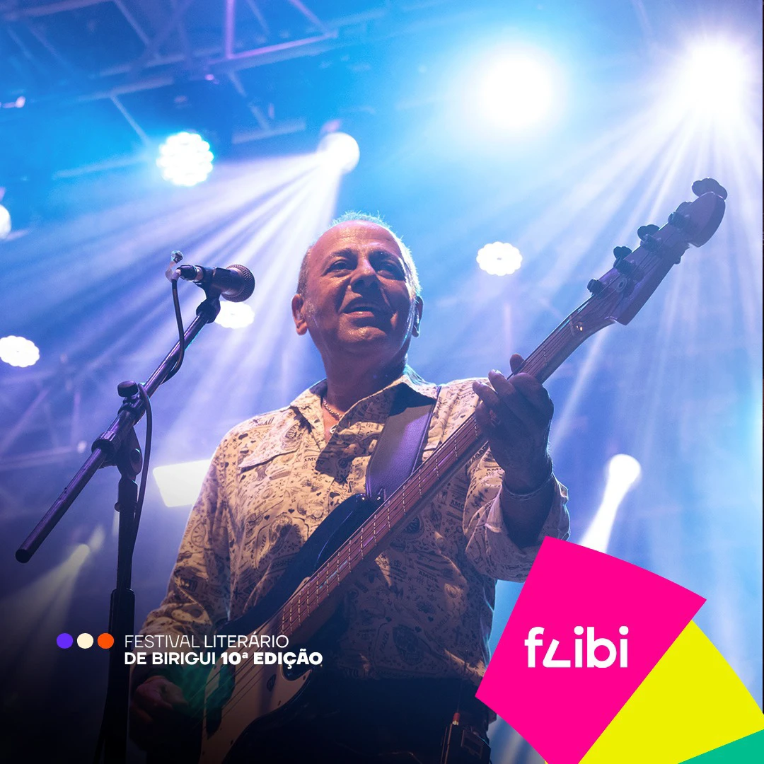 Baixista canta ao microfone no palco, iluminado por refletores azuis.