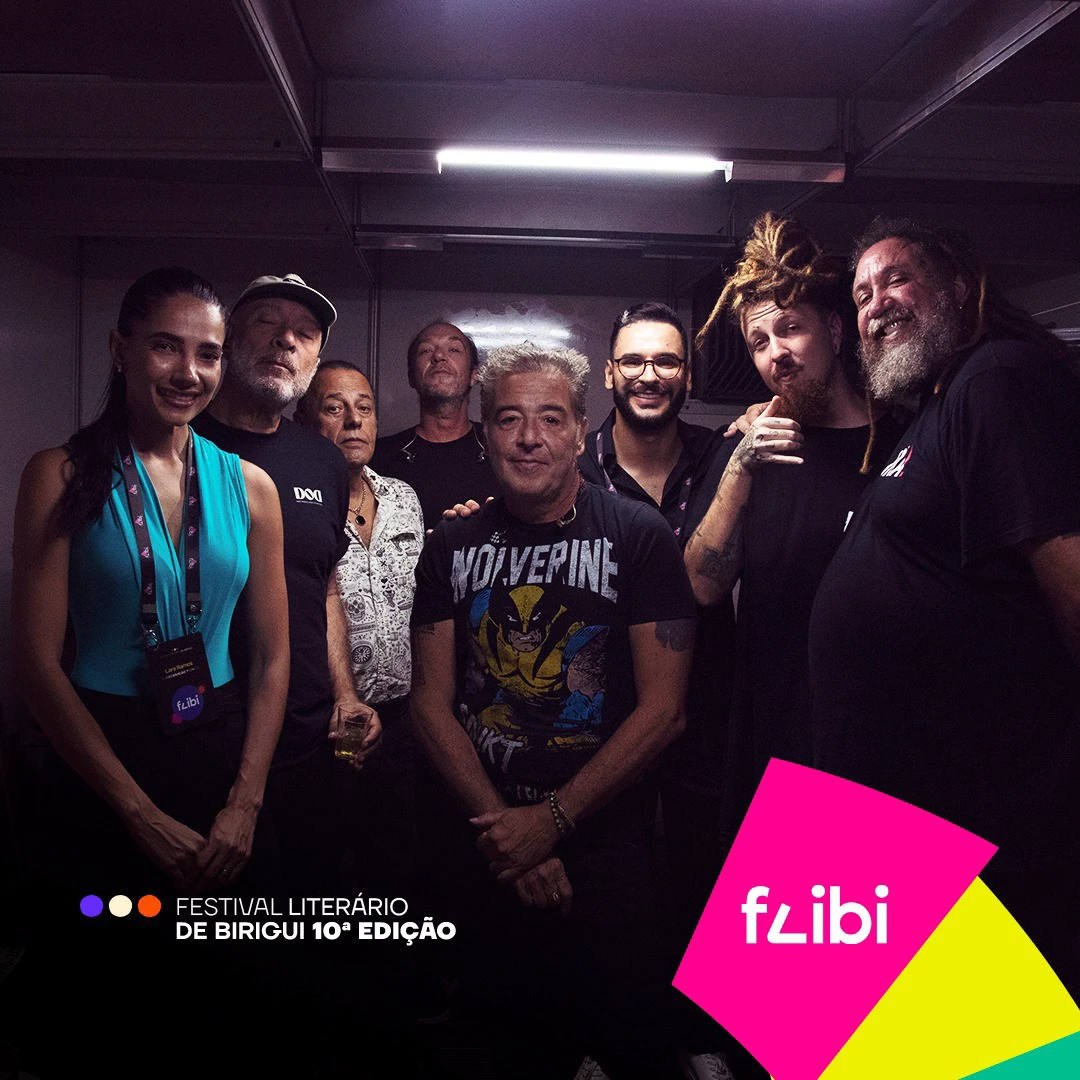 Foto de bastidores com a equipe do festival e os integrantes da banda reunidos em um camarim.