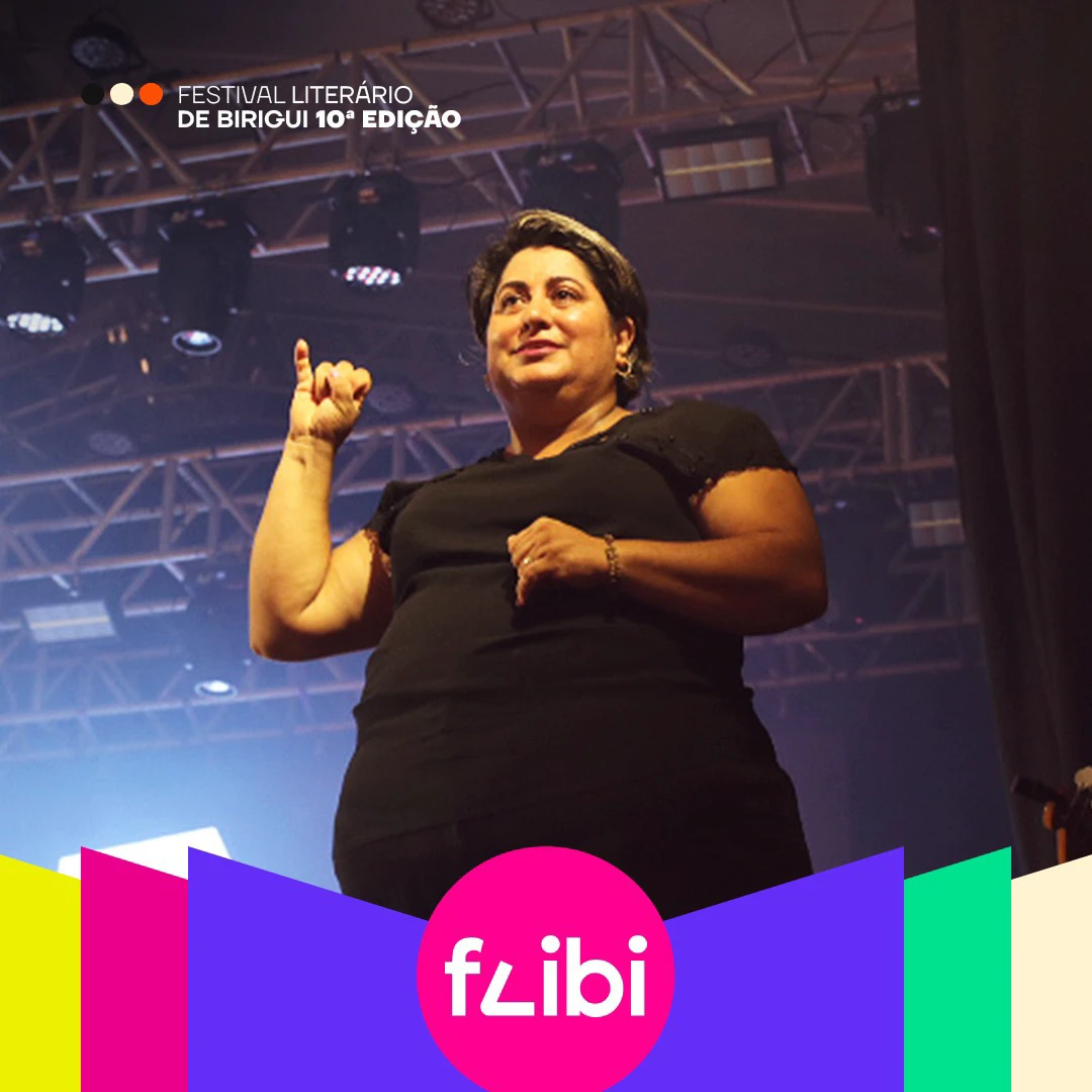 Intérprete de Libras traduz uma apresentação no palco, sob a estrutura de luzes.