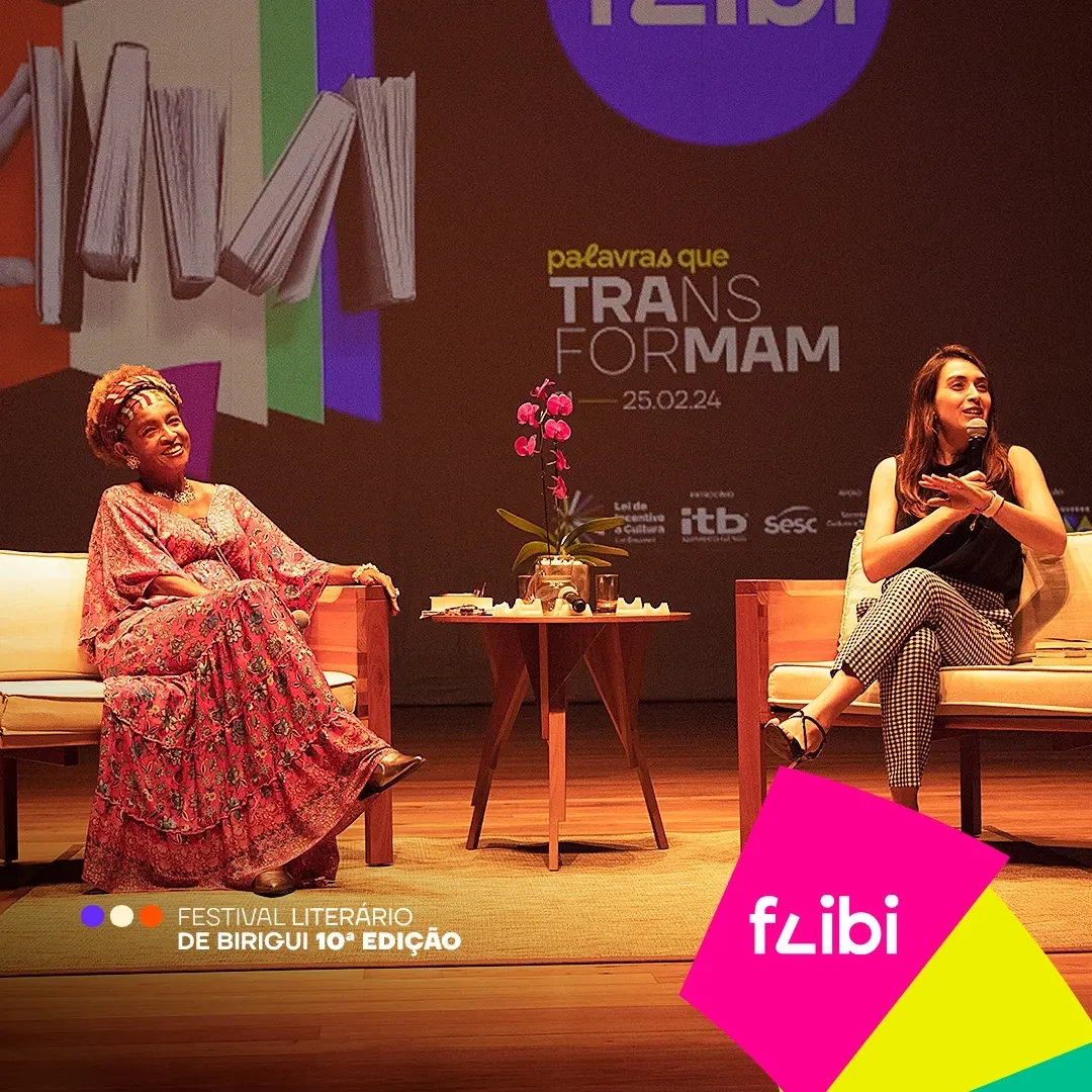 Elisa Lucinda e a mediadora conversam no palco, diante do painel com a colagem de livros e a chamada “palavras que transformam”.