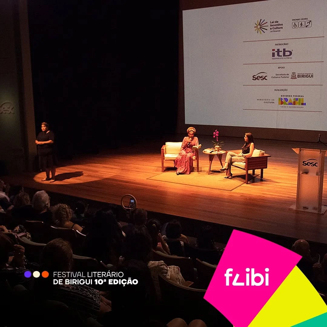 Mesa literária no palco do Teatro Sesc, com duas convidadas sentadas em poltronas e a plateia lotada em primeiro plano.