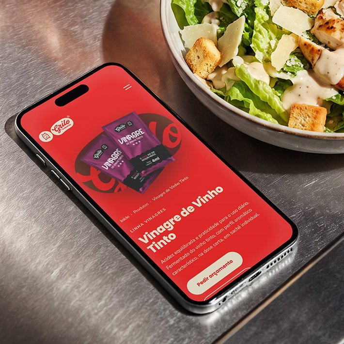 Página do Vinagre de Vinho Tinto aberta no celular, sobre bancada de inox ao lado de uma salada Caesar