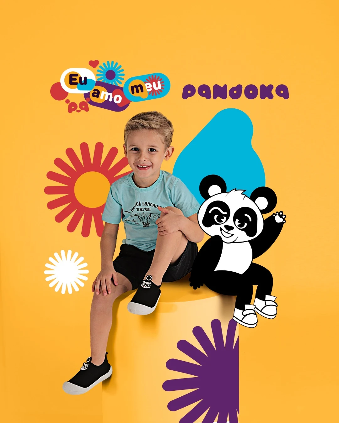 Post da Pandoka: menino de camiseta azul sentado num cubo amarelo, ao lado do mascote, com o selo “Eu amo meu pa” e explosões coloridas.