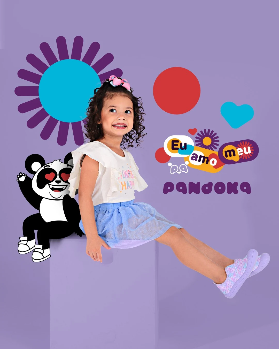 Post da Pandoka: menina de blusa branca e saia azul sentada num cubo lilás, entre dois mascotes, com o selo “Eu amo meu pa”.