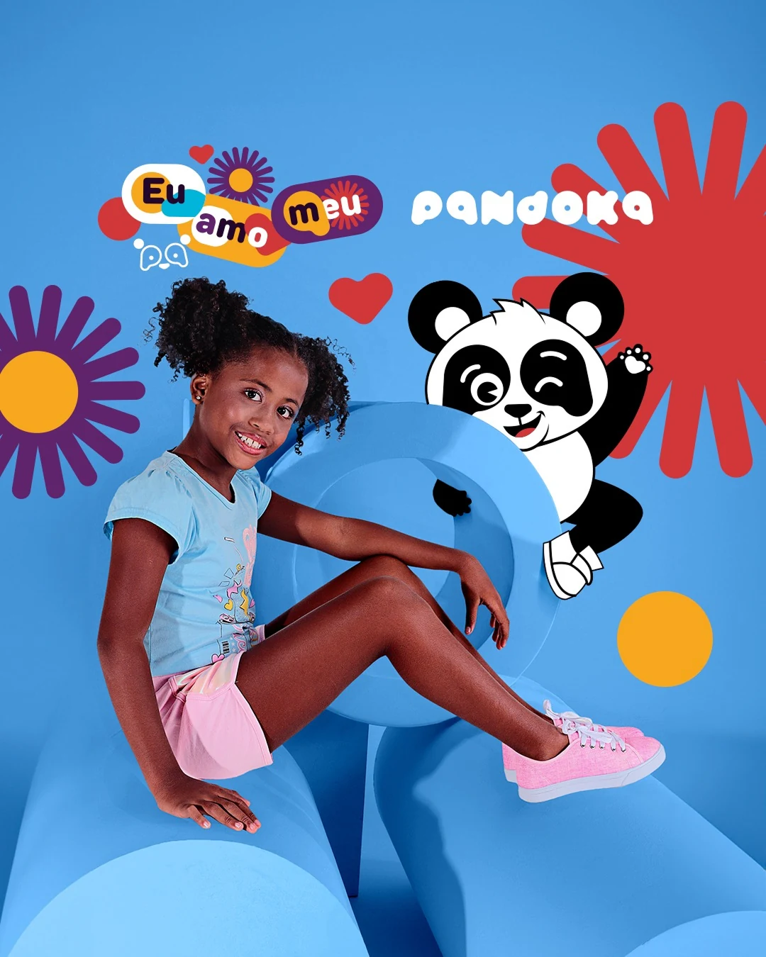 Post da Pandoka: menina de camiseta azul-clara recostada numa forma azul, ao lado do mascote, com o selo “Eu amo meu pa” e flores coloridas.