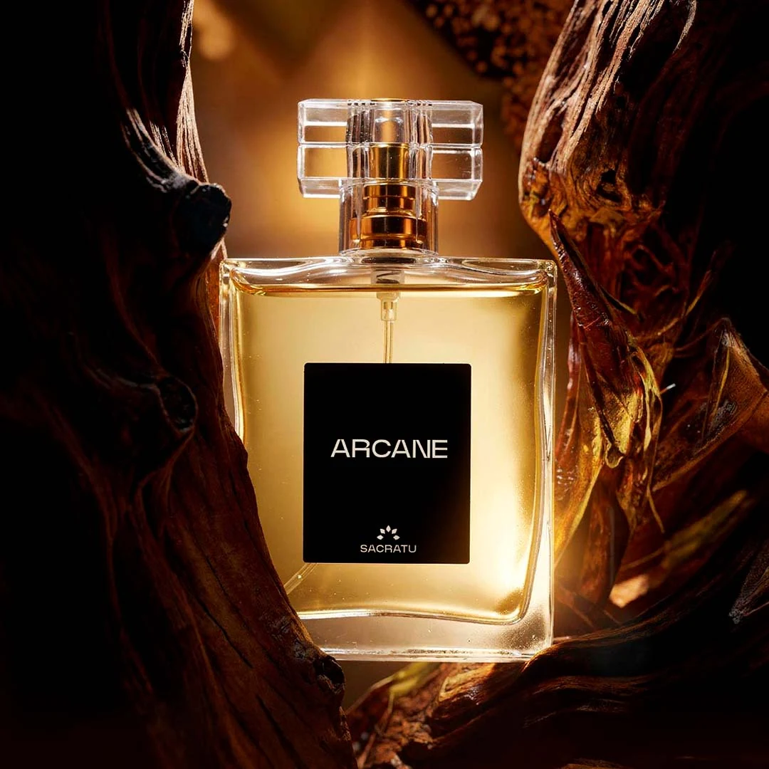 Frasco do perfume Arcane, da Sacratu, em luz âmbar sobre madeira retorcida e especiarias.