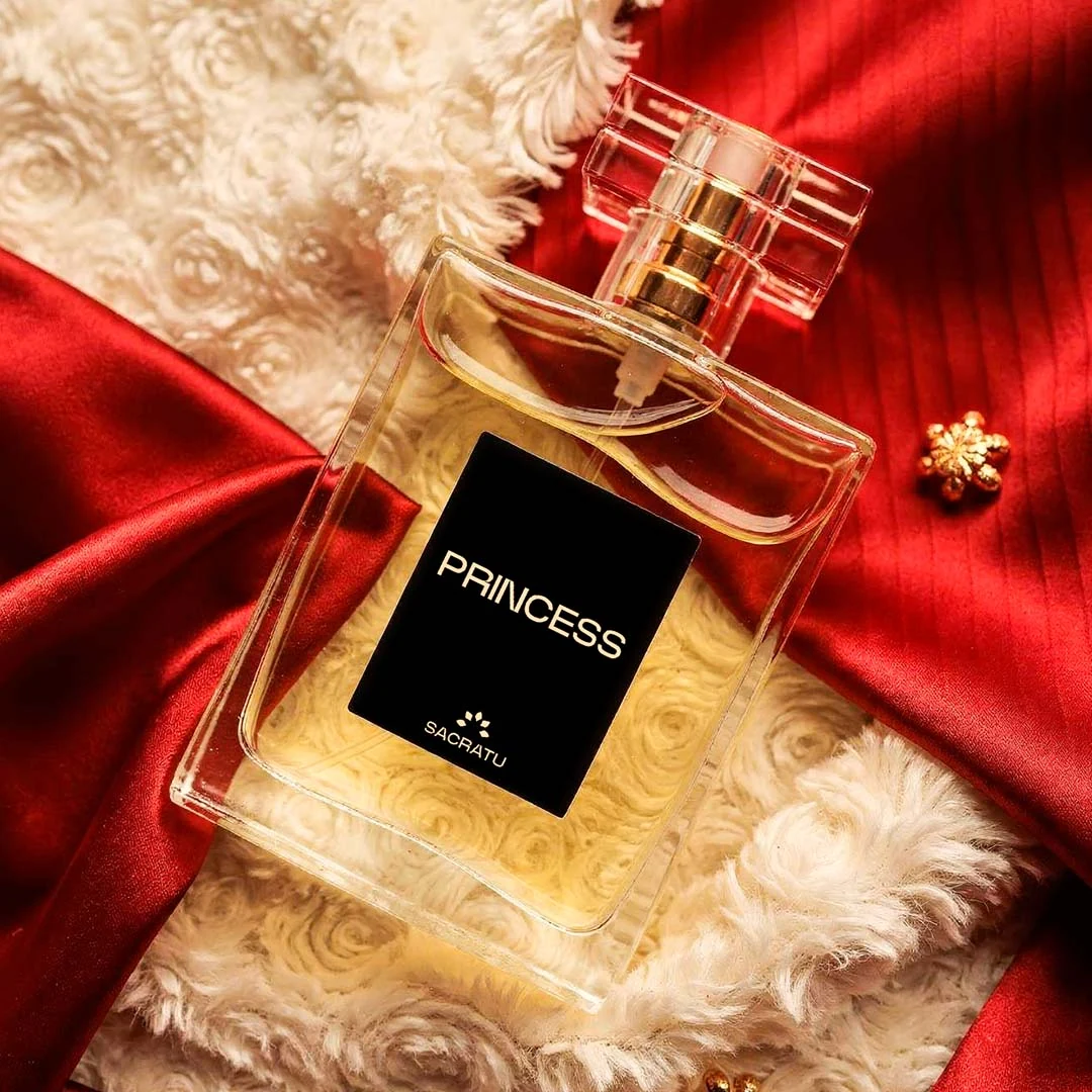 Frasco do perfume Princess, da Sacratu, deitado sobre cetim vermelho e pelo branco.