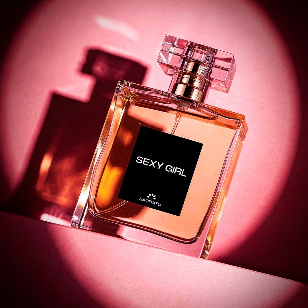 Frasco do perfume Sexy Girl, da Sacratu, em degradê rosa e laranja sob um círculo de luz rosa.