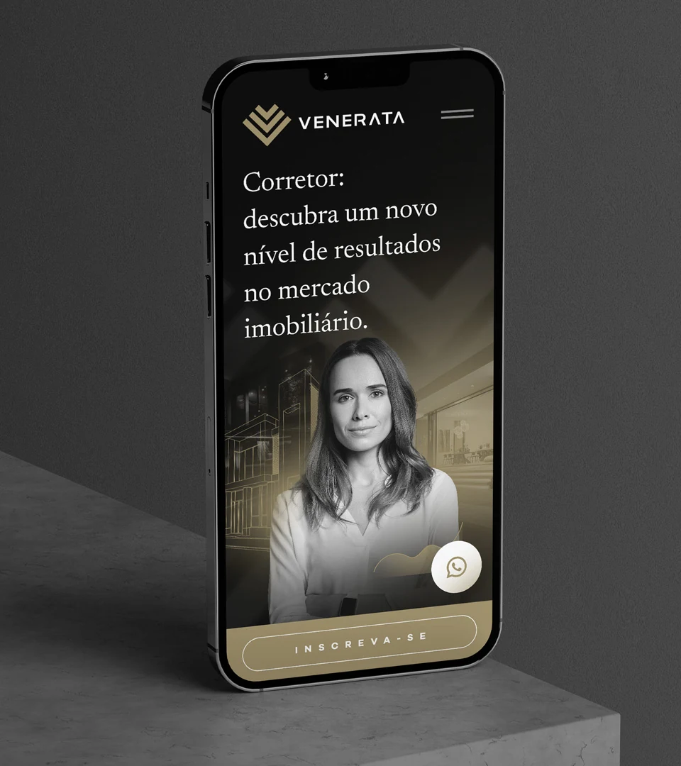 A landing page da Venerata num celular apoiado sobre concreto: a mesma chamada para corretores, a foto da mentora e o botão de inscrição, em preto e dourado.
